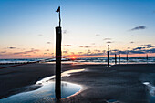 Sunset by the North Sea on the beach during low tide with wooden bollard in the foreground, Juist, Schleswig Holstein, Germany