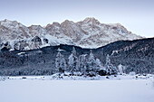 Baumbestandene Insel im zugefrorenen Eibsee, Blick zur Zugspitze, bei Grainau, Bayern, Deutschland