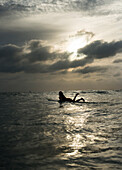 A female surfer paddles out as the sun sets at Newport Beach, Calif.