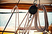Foreground of pulley and ropes and the boom and mainsail in the background of a vintage yacht moored at Port Mahón, Menorca, Balearic Islands, Spain, Europe