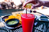 Frozen Strawberry daiquiri on a table at an outdoor restaurant with a woman´s hand squeezing a lemon on top of the glass.