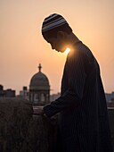 Man on roof / building terrace and Minarets at sunset, New Delhi, India.