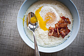 bowl of grits with bacon and egg on top.