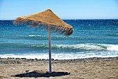 Rustic brown sun umbrellas made of natural fibers on a nice beach in Costa del Sol, Andalusia, Spain