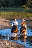 Two wranglers (cowboys) on horses, riding through water, California, USA