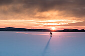 Einsamer Schlittschuhfahrer zieht die ersten Bahnen durch den Schnee auf dem Rangsdorfer See bei Sonnenuntergang - Deutschland, Brandenburg, Rangsdorf