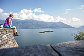 Junge Wanderin sitzt auf einer Mauer und blickt auf einen See, Ronco, Tessin, Schweiz