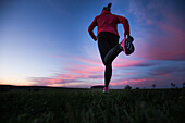Young woman running over a field at sunset, Allgaeu, Bavaria, Germany