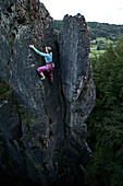 Junge Frau klettert an einer Felswand, Pottenstein, Franken, Deutschland