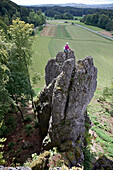 Junge Kletterin sitzt auf der Spitze eines hohen Felsens, Pottenstein, Franken, Deutschland