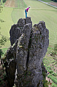 Young female climber standing on the top of a high rock, Pottenstein, Franconia, Germany