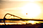 Blick über ein Segel am See zu einem Heißluftballon waehrend eines Sonnenuntergangs, Ammersee, Bayern, Deutschland