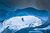 Young female freeskier jumping down from a cave of a glacier in the mountains, Pitztal, Tyrol, Austria