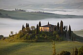 The Belvedere farmhouse in Val d’Orcia with early morning fog, San Quirico d´Orcia, Tuscany, Italy.
