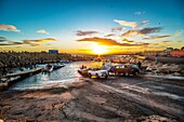 Small fishing boats ski boats are launched on a broad slipway as the sun rises over the sea. Cape Town, South Africa