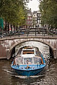 A tour boat passes under the Hemonybrug bridge at Keizersgracht and Leidsegracht in Amsterdam.