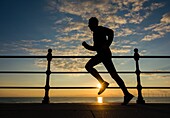 Male runner silhouetted against rising sun at Seaton Carew on the north east coast of England, United Kingdom.