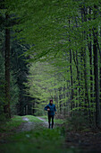 Junger Mann läuft auf einem Weg durch einen Wald, Allgäu, Bayern, Deutschland