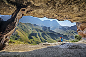 Woman hiking sitting in front of big cave, Pillar Cave, Garden Castle, Mzimkhulu Wilderness Area, Drakensberg, uKhahlamba-Drakensberg Park, UNESCO World Heritage Site Maloti-Drakensberg-Park, KwaZulu-Natal, South Africa