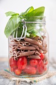 Glass jar with ingredients for pasta with tomato and basil.