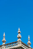 A balcony with stone railings and stone obelisks on a historical building in front of a blue sky, Granada, Andalusia, Spain