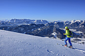 Frau auf Skitour steigt zum Hochgern auf, Kaisergebirge im Hintergrund, Hochgern, Chiemgauer Alpen, Oberbayern, Bayern, Deutschland