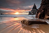 The fiery sky at sunset is reflected on the fine sand of Praia da Ursa beach Cabo da Roca Colares Sintra Portugal Europe.