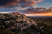 Dawn light illuminates the houses and buildings of Gordes as they spiral up around the rock plateau high above the Luberon, Vaucluse, Provence, France, Europe