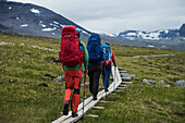 Hikers walk on wooden planks between Alesjaure and Tjäktja, Kungsleden trail, Lapland, Sweden
