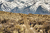 A young woman rides a mountain bike down a dirt road with snow-covered mountains in the distance
