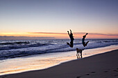 Happy couple with a dog jumping high on an Australian beach at Sudnrise, Numbucca Heads, Australia