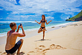 Young man making a photo of pretty woman on a beach