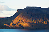 'Late day sun illuminates the steep tiered cliffs in Iceland's Westfjords; Westfjords, Iceland'