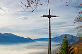 'A cross in the foreground and fog over a city and alpine lake; Locarno, Ticino, Switzerland'