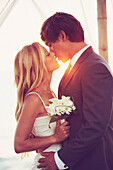 Beautiful Sunset Wedding by the Sea. Bride and Groom Kissing at Sunset. Romantic Married Couple.