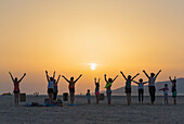 'A group of women with some children doing yoga on a beach at sunset; Tarifa, Andalusia, Spain'