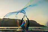 'A man uses wands to create large bubbles in Hanalei Bay; Kauai, Hawaii, United States of America'