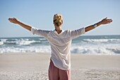 Beautiful young woman with arm outstretched on sunny beach