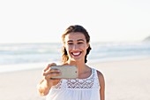 Beautiful young woman taking selfie with smartphone on the beach