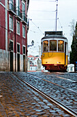 Yellow tram number 28 passes in Alfama district characterized by a typical architecture on a rainy day Lisbon Portugal Europe