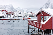 Icy sea and snowy peaks around the typical houses called rorbu and fishing boats Hamn?©y Lofoten Islands Northern Norway Europe