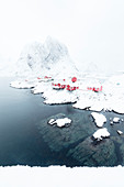 The snowy peaks and frozen sea frame the typical fisherman houses called Rorbu Hamn?©y Lofoten Islands Northern Norway Europe