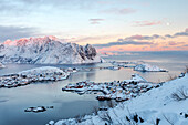 The pink colors of sunset and snowy peaks surround the fishing villages Reine Nordland Lofoten Islands Norway Europe
