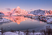 Snowy peaks are reflected in the frozen sea at sunset Reine Bay Nordland Lofoten Islands Norway Europe