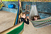 Caucasian brother and sister laying in hammocks holding hands