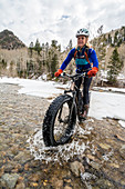 A woman riding her fat tire bike across a creek in La Plata Canyon, Mayday, Colorado.