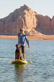 A woman and her dog paddleboarding on Lake Powell, Wahweap Marina, Glen Caynon National Recreation Area, Page,  Arizona.
