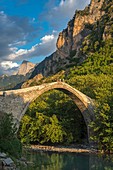 The old stone bridge across the Aoos river at Konitsa with Mount Tymfi in the background, Epirus, Northern Greece.