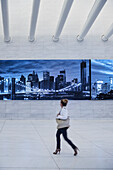 woman passing a lit advertisement in a corridor of the Oculus and looks at the Skyline of New York, futuristic train station by famous architect Santiago Calatrava next to WTC Memorial, Manhattan, New York City, USA, United States of America