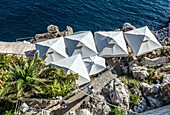 restaurant umbrellas on the rocks under the Old Town Walls of Dubrovnik in Croatia.